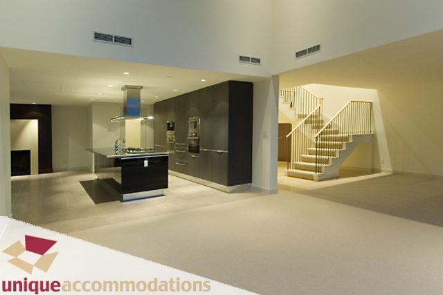 Modern kitchen with dark cabinetry and stainless steel appliances, leading to a staircase with wooden banister.