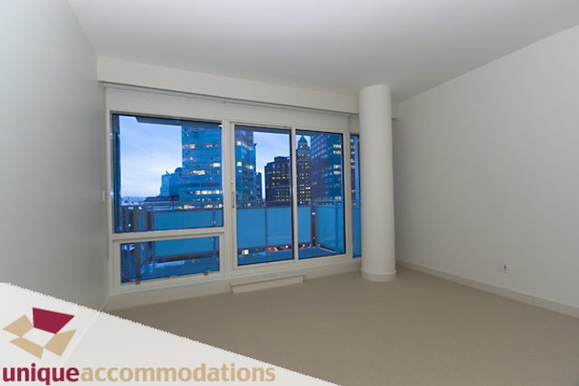 Bright living room with large windows showcasing city skyline, modern furnishings, and white walls.