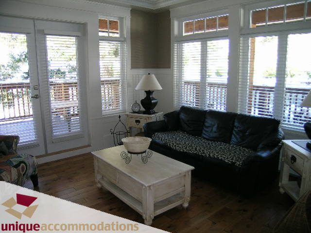 Bright living room with hardwood floors, large windows, and a cozy black leather couch. - 3290 St. Georges Ave, North Vancouver