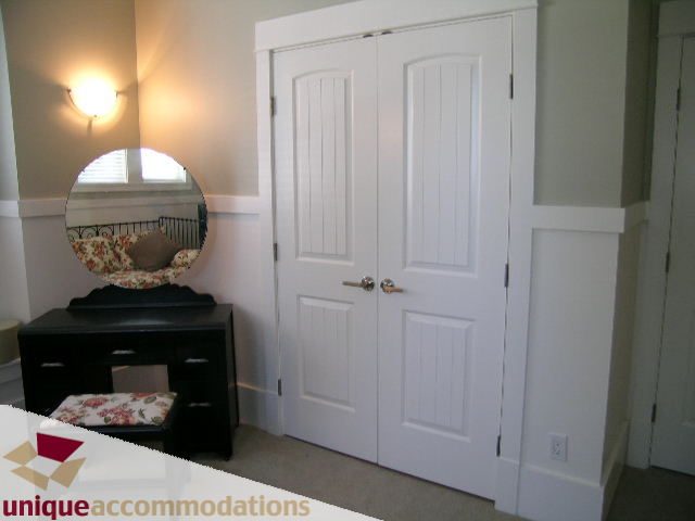 Bright bedroom with white closet doors, floral bedding, and wall sconce lighting. - 3290 St. Georges Ave, North Vancouver