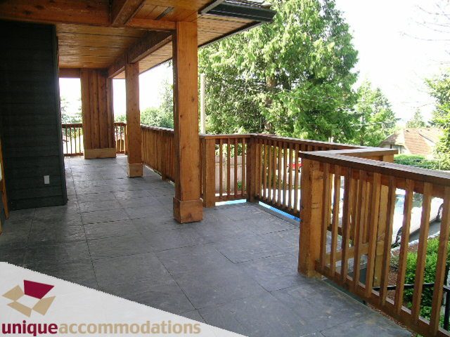 Furnished balcony with wooden railings and stone flooring, offering a view of greenery. - 3290 St. Georges Ave, North Vancouver