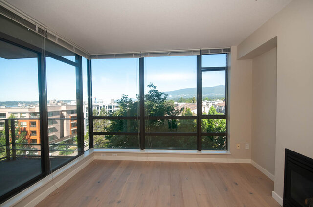 Spacious living room with panoramic city views through floor-to-ceiling windows and light wood flooring. - 606 - 170 1st Street West, North Vancouver