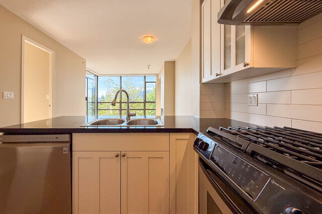 Kitchen with dark granite countertops, white shaker cabinets, and a gas range beside a window with a treetop view.