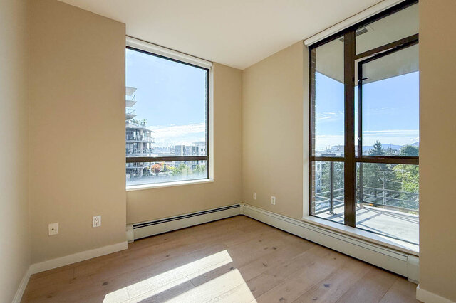 Bright bedroom with light hardwood floors and large corner windows framing a water and skyline view. - 606-170 1st Street West, North Vancouver