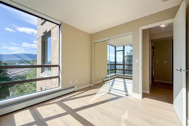 Sunlit bedroom with light hardwood floors, a mirrored closet, and a large window framing a mountain view. - 606-170 1st Street West, North Vancouver