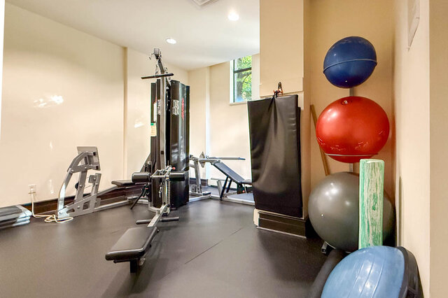 Compact home gym with rubber flooring, a cable machine, weight bench, and a stack of colorful stability balls.
