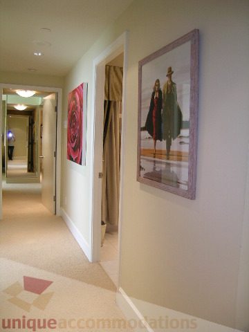 Framed artwork decorates the hallway leading to a bedroom, featuring a man in a trench coat. - 802 - 323 Jervis Street, Vancouver Downtown