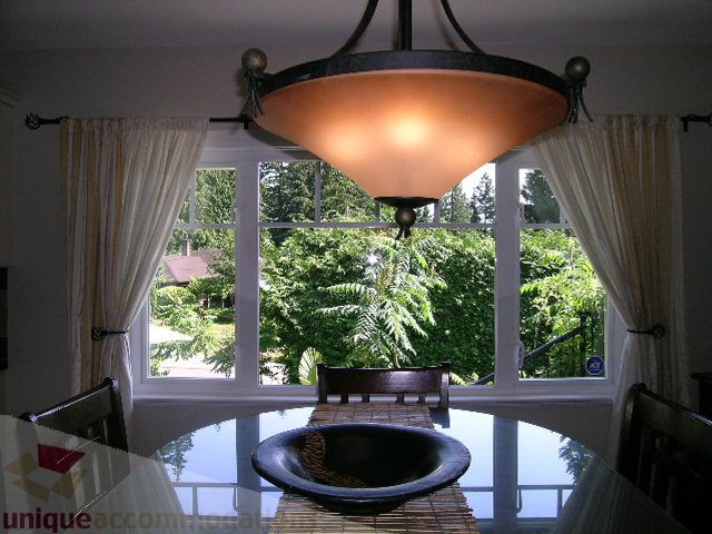 Dining room with large windows, lush greenery view, modern chandelier. - 4104 Sunnycrest drive, North Vancouver