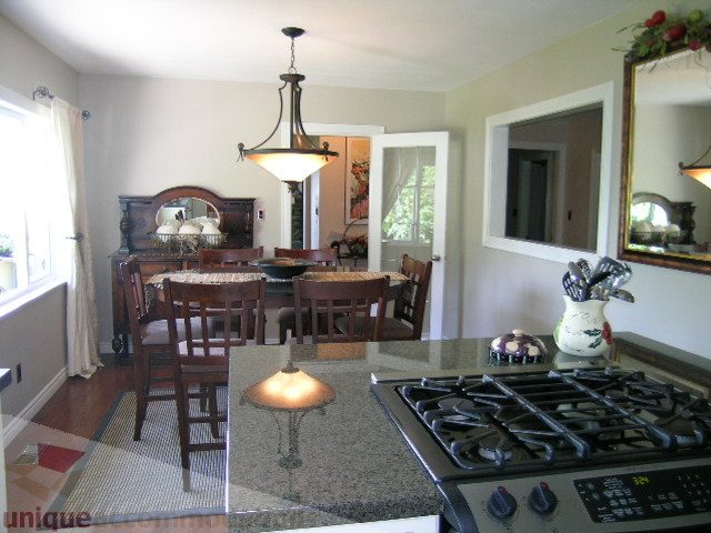 Bright kitchen with granite countertops and gas stove, open to dining area with wooden table and chairs. - 4104 Sunnycrest drive, North Vancouver