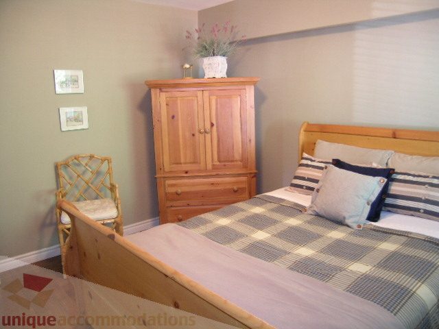 Furnished bedroom with wooden furniture, checkered bedding, and a bamboo chair. - 4104 Sunnycrest drive, North Vancouver