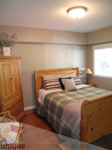 Bright bedroom with wooden furniture and plaid bedding, natural light from window. - 4104 Sunnycrest drive, North Vancouver