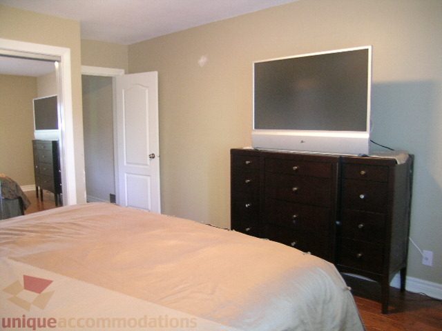 Master bedroom with large bed, dark wood furniture, and flat-screen TV mounted on wall. - 4104 Sunnycrest drive, North Vancouver