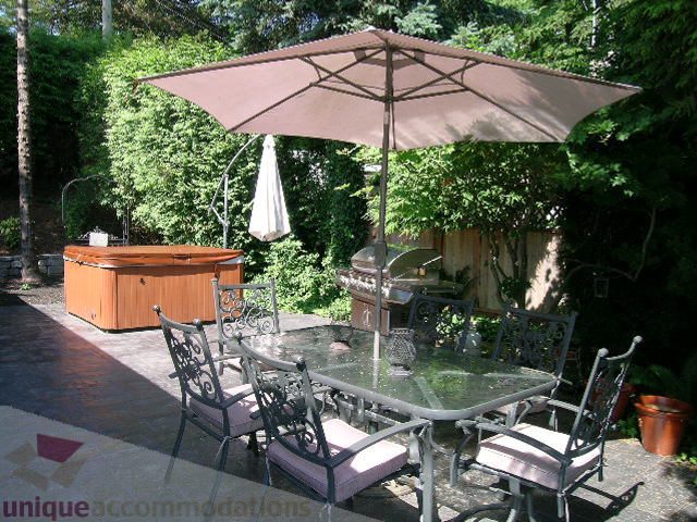 Furnished patio with glass table, chairs, and umbrella, surrounded by lush greenery. - 4104 Sunnycrest drive, North Vancouver