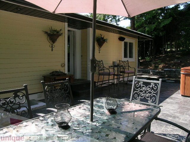 Furnished patio with glass-topped table and wrought iron chairs, surrounded by lush greenery. - 4104 Sunnycrest drive, North Vancouver