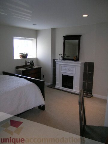 Bright bedroom with large window, white bedding, and fireplace. - 4104 Sunnycrest drive, North Vancouver