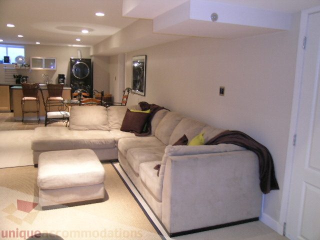 Furnished living room with white couches, modern decor, and kitchen in background. - 4104 Sunnycrest drive, North Vancouver