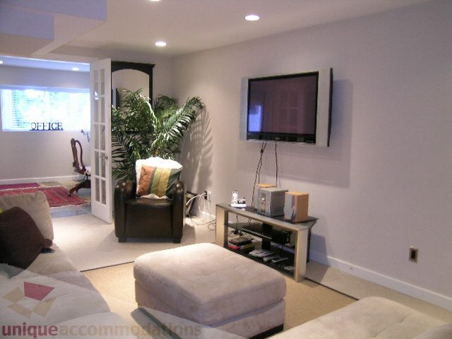 Living room with a mounted TV, cozy seating, and a large ottoman. - 4104 Sunnycrest drive, North Vancouver
