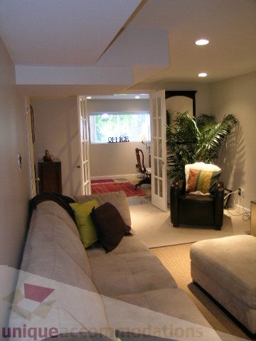 Furnished living room with a cozy sofa, decorative pillows, and a view of the kitchen. - 4104 Sunnycrest drive, North Vancouver