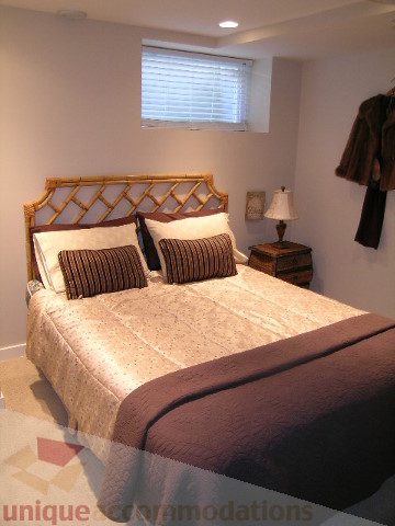 Furnished bedroom with bamboo headboard, patterned bedding, and window with blinds. - 4104 Sunnycrest drive, North Vancouver
