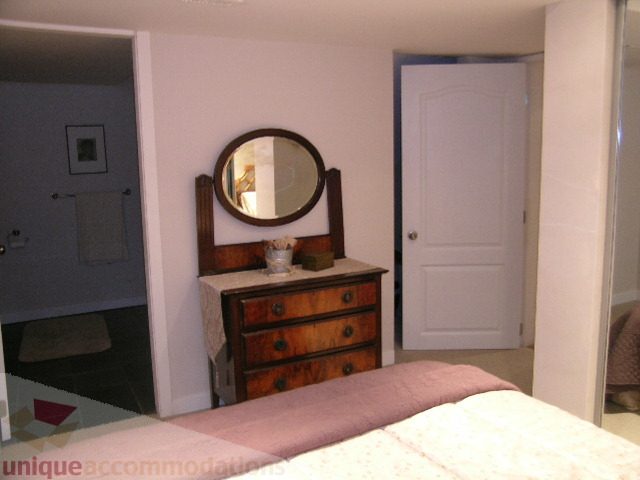 Furnished bedroom with wooden dresser and round mirror, light-colored walls. - 4104 Sunnycrest drive, North Vancouver