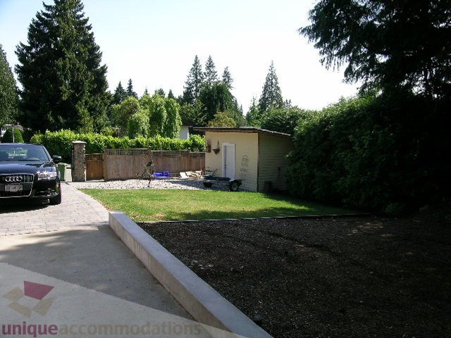 Fenced backyard with grass and shrubs, leading to a house with a green roof. - 4104 Sunnycrest drive, North Vancouver