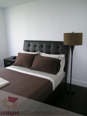 Furnished bedroom with tufted headboard, modern lamp, and dark wood flooring. - 705 - 1055 Homer Street, Vancouver Downtown