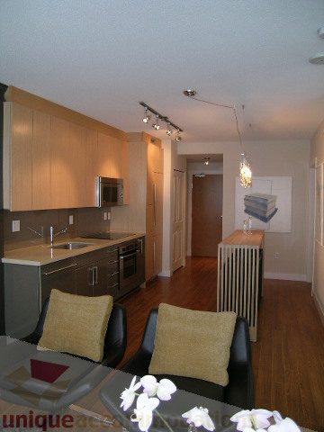 Bright kitchen with dark countertops and hardwood floors, adjacent to a cozy living area with a black leather chair and...