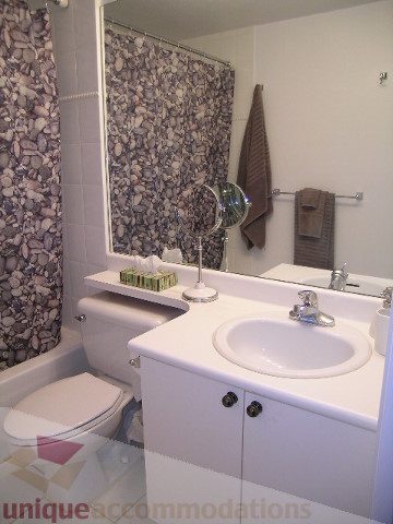 Bright bathroom with white countertop and modern sink, featuring a patterned shower curtain. - 405 - 233 Abbott Street, Vancouver Downtown