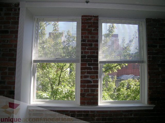 Bright living room with large windows, brick walls, and a view of greenery outside. - 405 - 233 Abbott Street, Vancouver Downtown