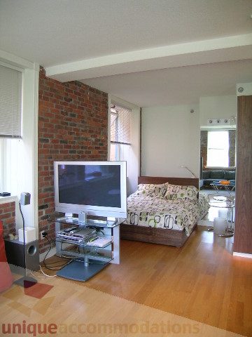 Bright living room with hardwood floors, brick accent wall, and modern furniture. - 405 - 233 Abbott Street, Vancouver Downtown