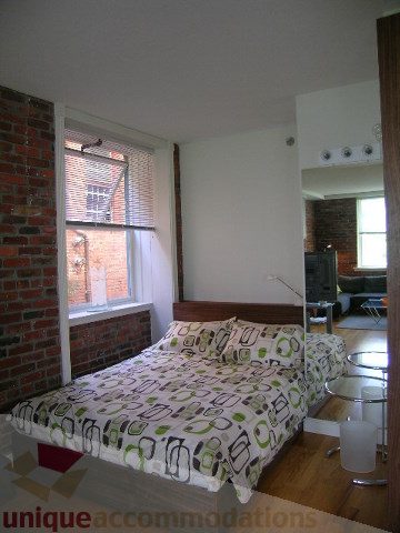 Bright bedroom with exposed brick walls, hardwood floors, and a city view. - 405 - 233 Abbott Street, Vancouver Downtown