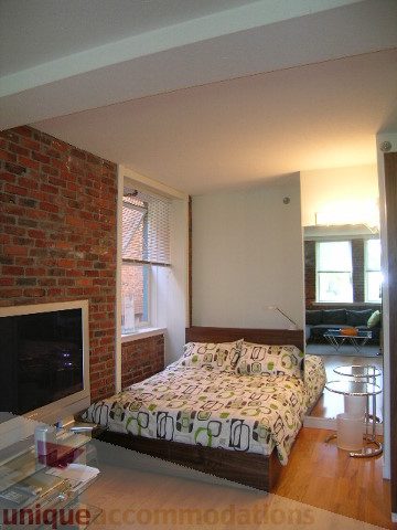 Furnished bedroom with brick wall, hardwood floors, and a cozy ambiance. - 405 - 233 Abbott Street, Vancouver Downtown