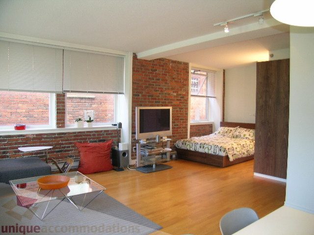 Furnished living room with hardwood floors, brick wall, and modern decor. - 405 - 233 Abbott Street, Vancouver Downtown