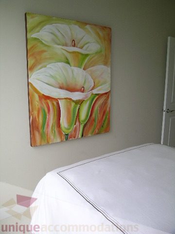 Bright bedroom with white bedding and vibrant floral artwork above the bed. - 102 - 1333 West 11th Ave., Vancouver West Side