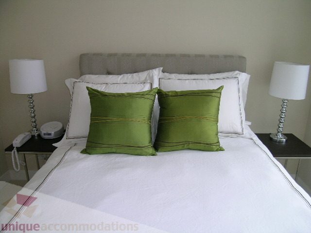 Bright bedroom with white bedding, green accent pillows, and bedside lamps. - 102 - 1333 West 11th Ave., Vancouver West Side