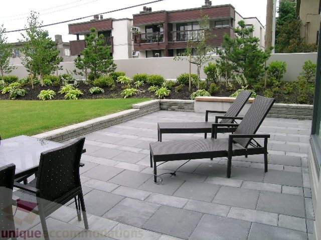 Furnished patio with lounge chairs and stone pavers, surrounded by greenery and buildings. - 102 - 1333 West 11th Ave., Vancouver West Side