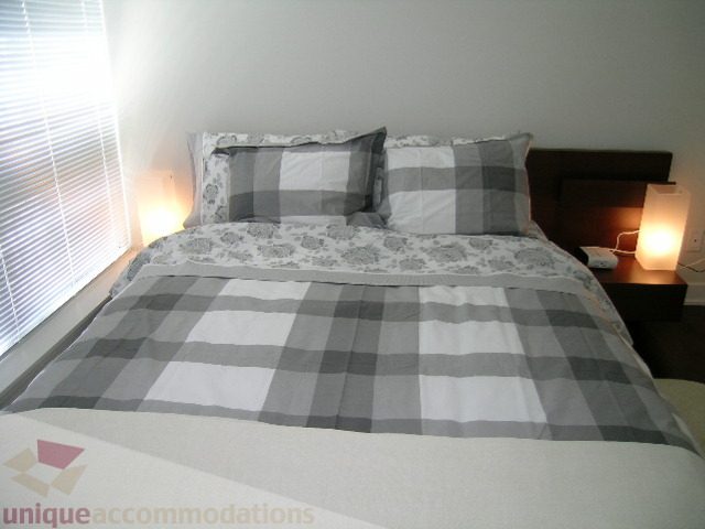 Spacious bedroom with checkered bedding and bedside lamps, perfect for a cozy stay. - 1209 - 1055 Richards Street, Vancouver Downtown