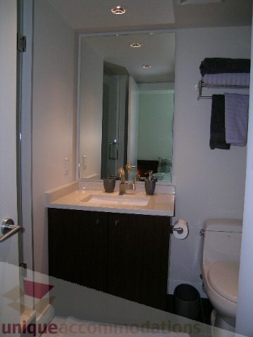 Modern bathroom with dark wood cabinets, white countertop, and a sleek sink setup. - 1209 - 1055 Richards Street, Vancouver Downtown