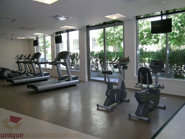 Spacious fitness room with large windows, treadmills, and exercise equipment, offering a serene city view.