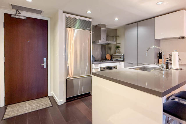 Modern kitchen with sleek white countertops, stainless steel appliances, and dark hardwood floors. - 1802 - 788 Richards, Vancouver Downtown