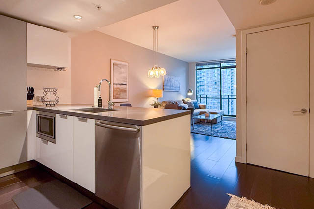 Modern kitchen with sleek countertops and hardwood floors, featuring a city view from the living area. - 1802 - 788 Richards, Vancouver Downtown