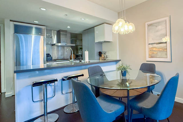 Modern kitchen with sleek countertops and a glass dining table with blue chairs. - 1802 - 788 Richards, Vancouver Downtown