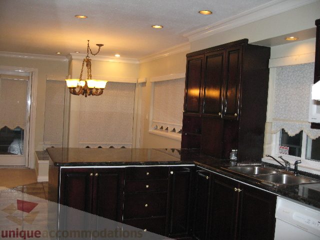 Bright kitchen with dark wood cabinets, granite countertops, and a chandelier. - 2737 Mahon Ave., North Vancouver