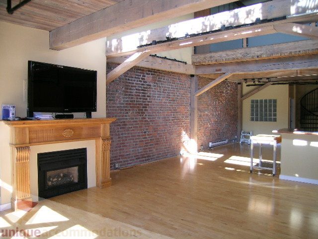 Bright living room with exposed brick wall, hardwood floors, and a large TV above a fireplace. - 408 - 1066 Hamilton Street, Vancouver Downtown