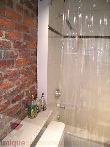 Furnished bathroom with brick wall and clear shower curtain. - 408 - 1066 Hamilton Street, Vancouver Downtown