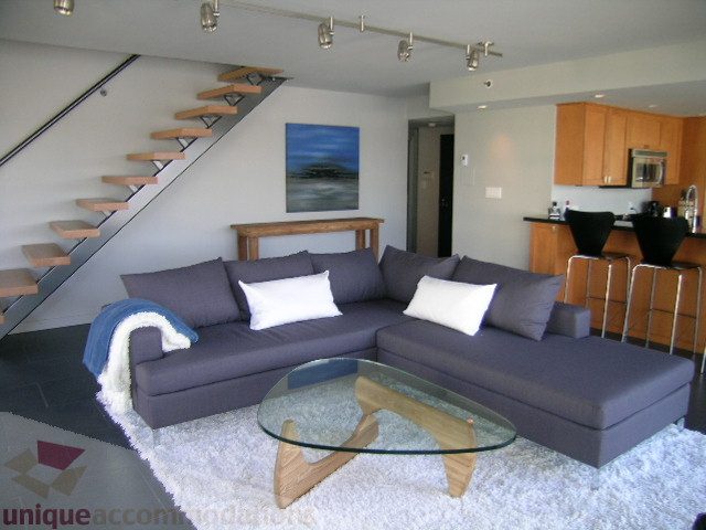 Living room with modern furniture, glass coffee table, and wooden staircase leading up. - 310 - 990 Beach, Vancouver Downtown