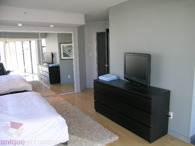 Bright bedroom with hardwood floors and a cozy rug, featuring a flat-screen TV and a neatly made bed. - 310 - 990 Beach, Vancouver Downtown