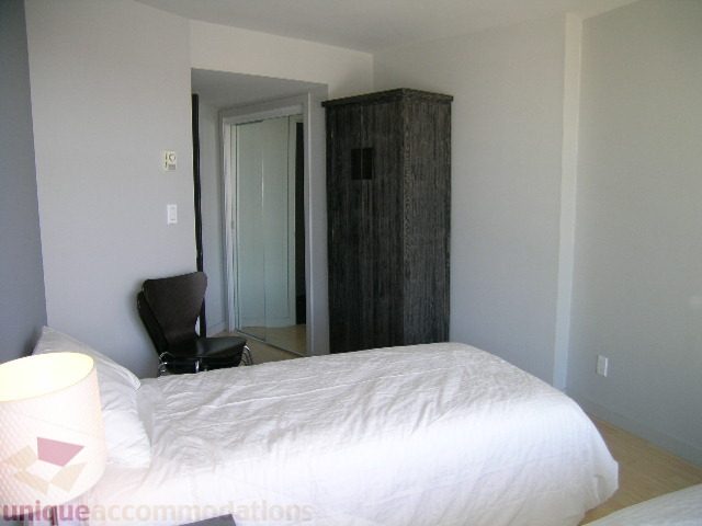 Bright bedroom with white bedding and wooden furniture, featuring a large closet and a bedside lamp. - 310 - 990 Beach, Vancouver Downtown