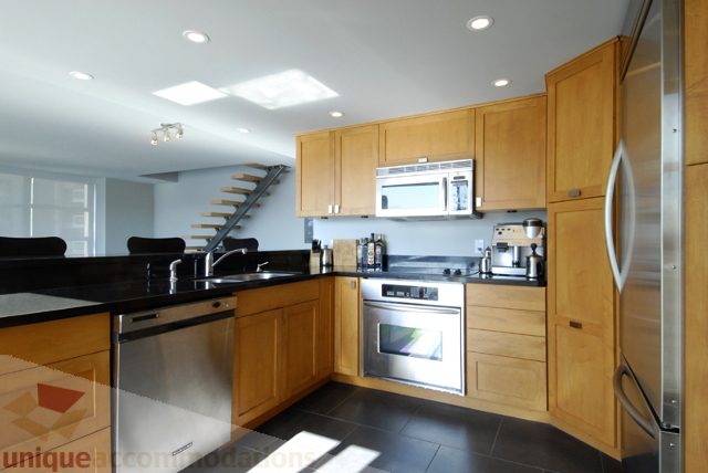 Bright kitchen with modern appliances, stainless steel fridge, wooden cabinets, and black countertops. - 310 - 990 Beach, Vancouver Downtown