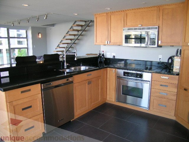 Bright kitchen with black countertops, stainless steel appliances, and a city view. - 310 - 990 Beach, Vancouver Downtown
